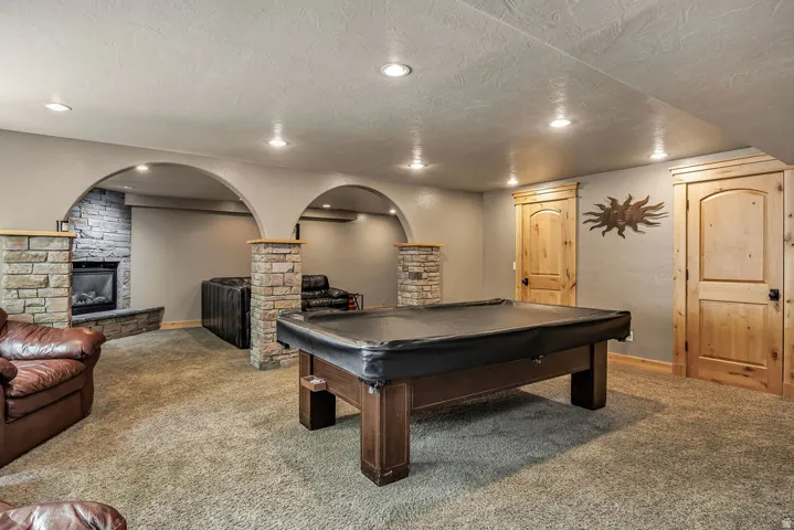 Expansive carpeted room featuring a stone fireplace with hearth, recessed lighting, and natural wood doors