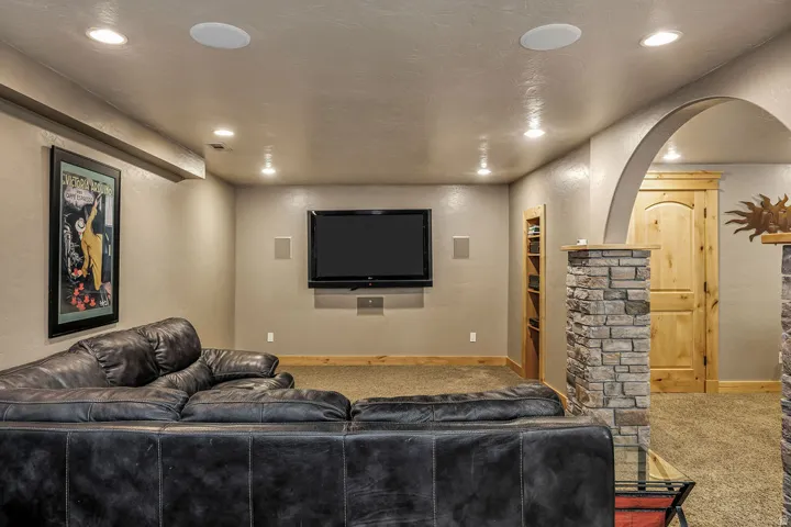 Entertainment room featuring recessed lighting, integrated ceiling speakers, a wall-mounted television, and an arched entry with stone-clad columns