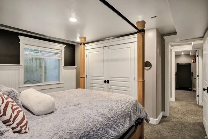 Recessed lighting illuminates this room featuring white wainscoting, a window with white blinds, and a built-in closet with white panel doors and black hardware