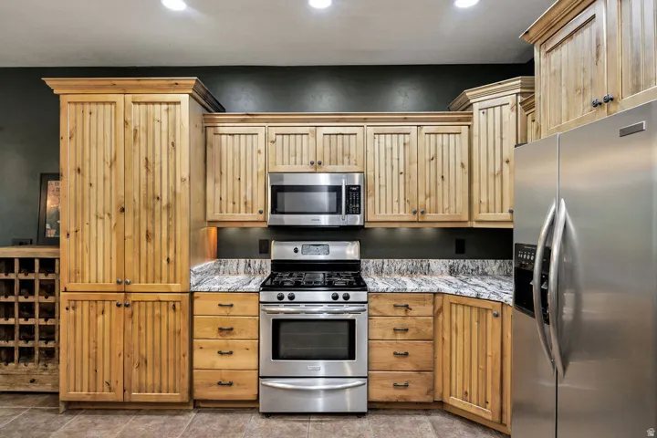 Kitchen featuring light wood cabinetry with beadboard paneling, stainless steel appliances, granite-style countertops, and tile flooring