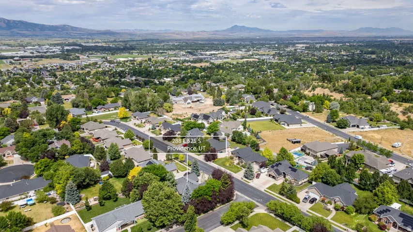 Residential streetscape featuring single-family homes, mature trees, and a paved road network