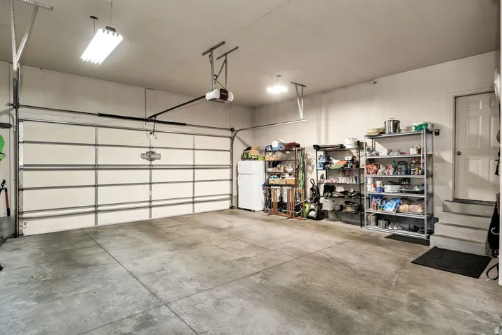 Spacious garage featuring a concrete floor, overhead fluorescent lighting, and an automatic garage door opener