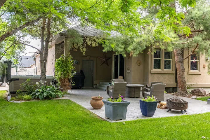 Expansive concrete patio with integrated hot tub, mature trees, stucco exterior, and sliding glass door access