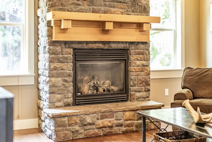 Stone-clad fireplace featuring a gas insert, a substantial wood mantel, a matching stone hearth, and wood-finish flooring