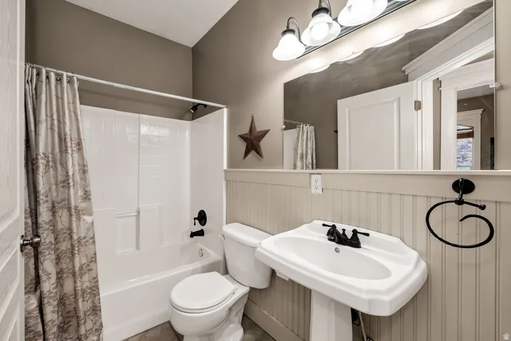 Bathroom featuring a white pedestal sink with black fixtures, a white toilet, and a white tub/shower combination with black fixtures