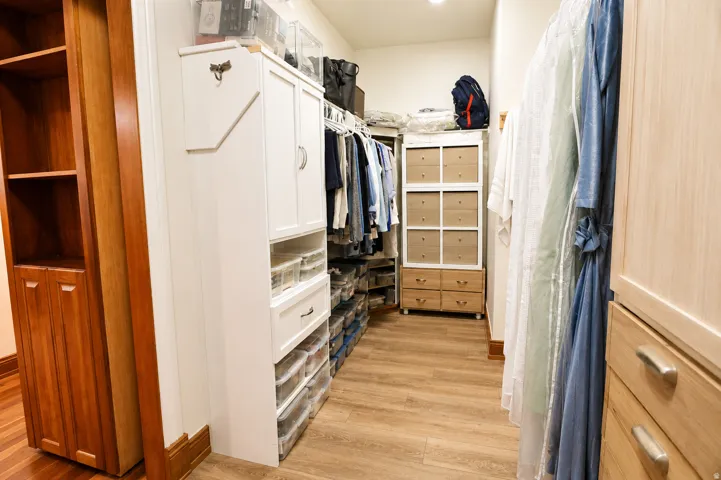Walk-in closet featuring extensive built-in cabinetry, wood-finish flooring, recessed lighting, and a blend of white and natural wood storage solutions