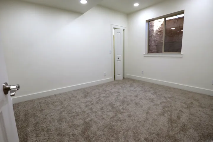 Room featuring neutral carpeting, white walls, recessed ceiling lighting, a window with a rock-lined outdoor area, and a white interior door