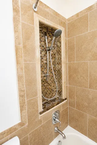 Bathtub shower combination featuring large format wall tiling, a mosaic-tiled shower niche with a stone shelf, and a polished chrome faucet and shower head