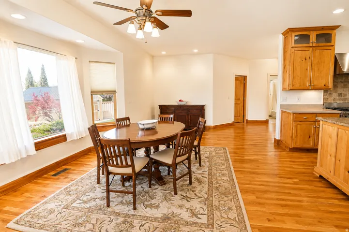 Open-concept dining area featuring wood-finish flooring, a bay window with natural wood trim, recessed lighting, and a ceiling fan
