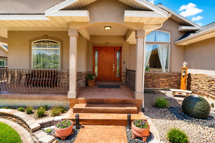 Stucco exterior featuring a covered entry, stone veneer accents, and an ornate wooden front door with sidelights