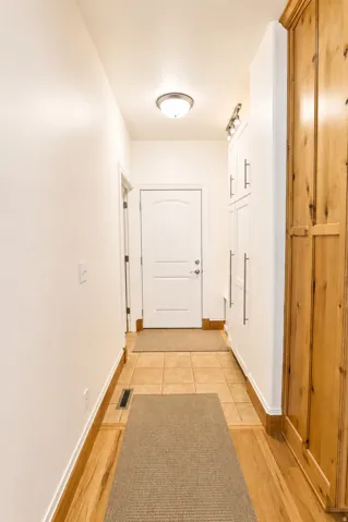 Hallway featuring wood-finish flooring, ceramic tile, white baseboards, and built-in white cabinetry with brushed nickel hardware