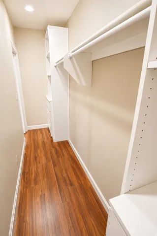 Organized closet system featuring wood-finish flooring, built-in shelving, integrated drawers, and multiple hanging rods