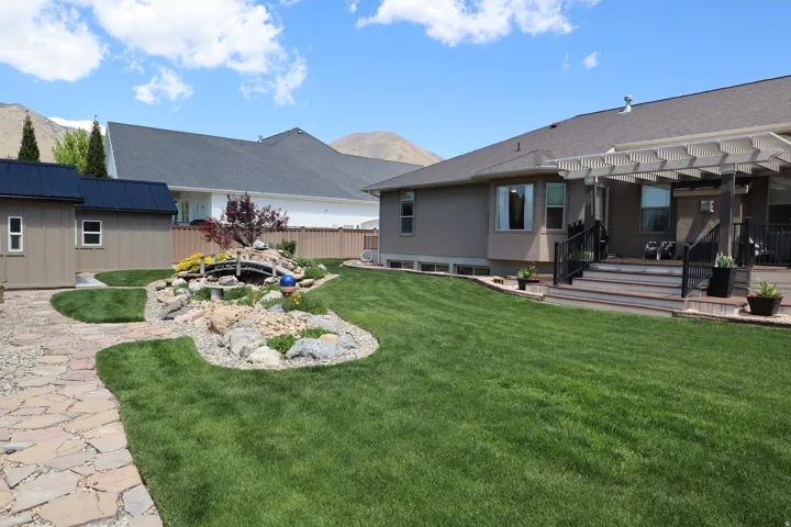 Expansive backyard featuring a lush lawn, flagstone pathway, and a decorative rock garden with a small bridge feature