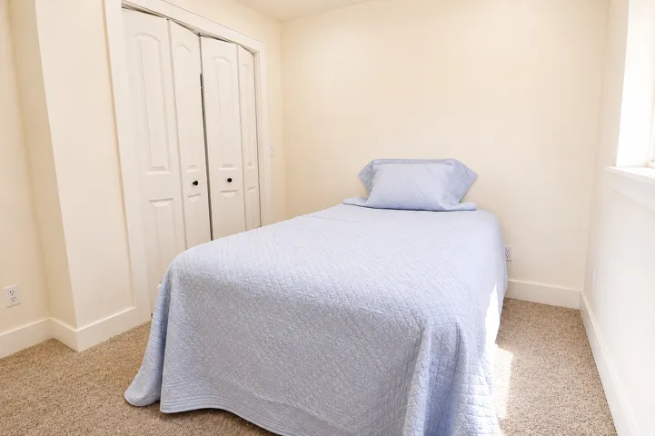 Bedroom featuring neutral carpeting, a window with white trim, and bi-fold closet doors with black hardware