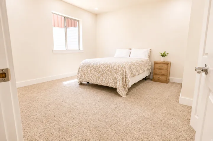 Carpeted room featuring a window with a white frame and blinds, light cream wall paint, and white baseboards