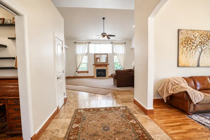 Entryway featuring tile flooring, leading to a living area with a vaulted ceiling and a fireplace with a wood mantle