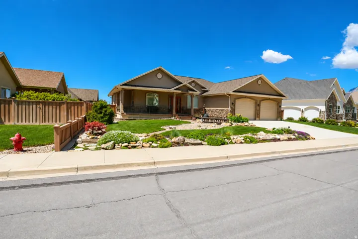 Stucco and stone exterior featuring a covered front porch, an attached two-car garage, and a landscaped front yard with mature plantings