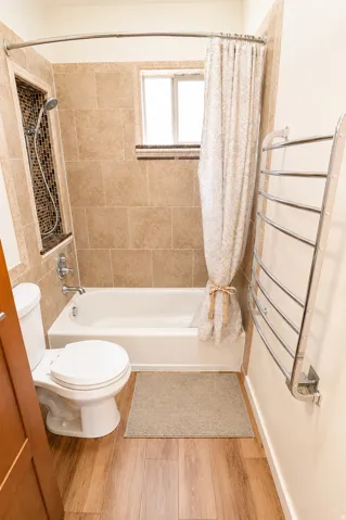 Bathroom featuring a tub and shower combination with custom tile surround, a mosaic-tiled shower niche, a window with frosted glass, and wood-finish flooring