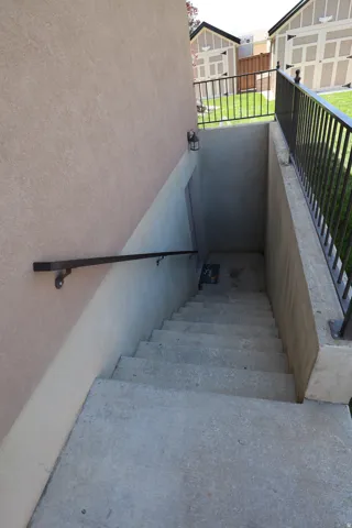 Exterior concrete stairs featuring a black metal handrail and a stucco-finish wall
