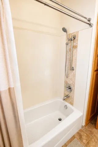 Bathtub and shower combination featuring a tiled accent wall and chrome fixtures