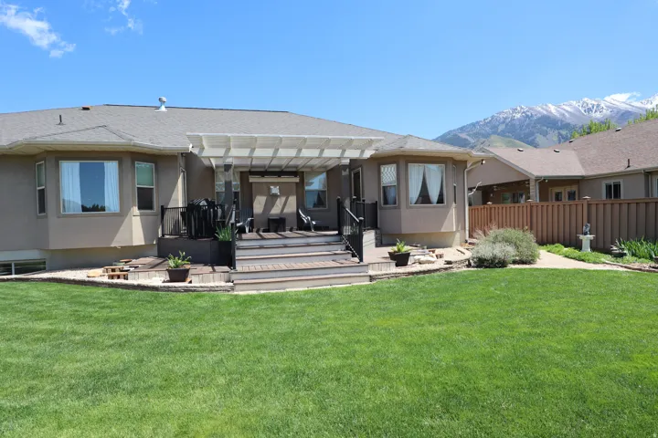 Expansive backyard featuring a manicured lawn, multi-level wood-finish deck with integrated steps, and a pergola-covered patio area