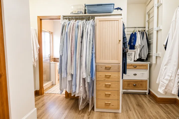 Walk-in closet featuring wood-finish flooring, built-in cabinetry with drawer storage, and extensive hanging rods