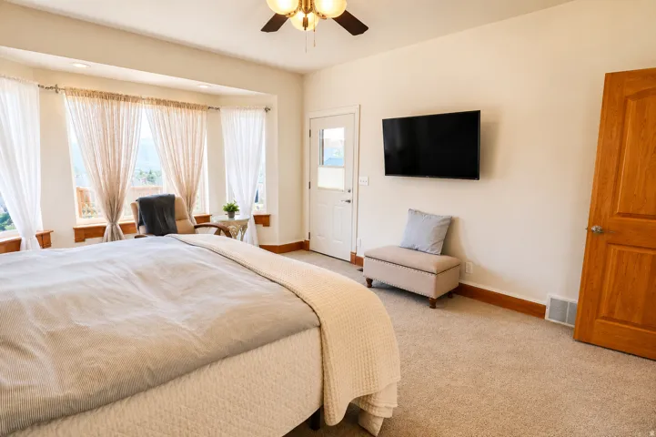 Carpeted room featuring a ceiling fan, a wall-mounted television, and a bay window with a door providing exterior access