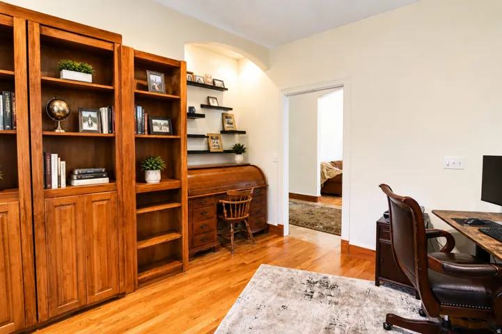 Hardwood flooring throughout featuring built-in wood cabinetry, integrated shelving, and an arched doorway