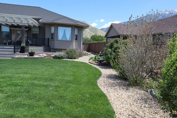 Expansive backyard featuring a manicured lawn, a gravel pathway, and a two-tier deck with a pergola