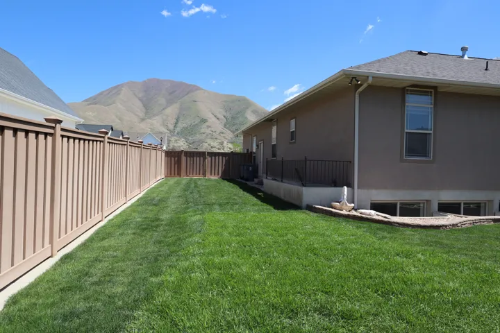 Expansive backyard featuring a manicured lawn, a full privacy fence, and a stucco exterior
