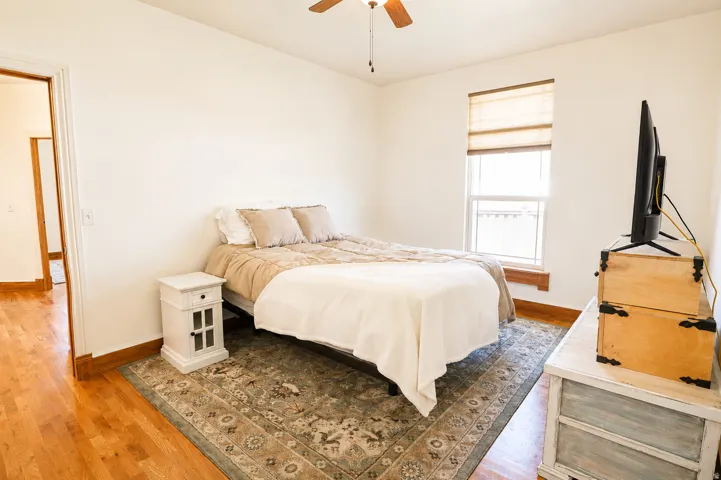 Bedroom featuring a ceiling fan, wood-finish flooring, a single window, and a doorway opening to a hallway with matching wood-finish flooring