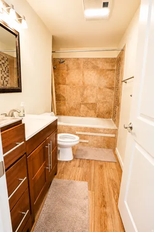 Bathroom featuring a wood-finish flooring, a full vanity with a white countertop, a bathtub with a tiled surround, and a coordinating tiled accent wall