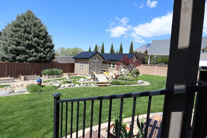 Expansive backyard featuring a green lawn, wood fence, and a storage shed with a dark metal roof