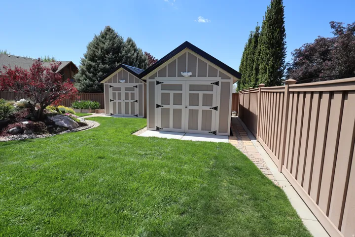 Expansive green lawn with two detached storage sheds featuring gambrel roofs