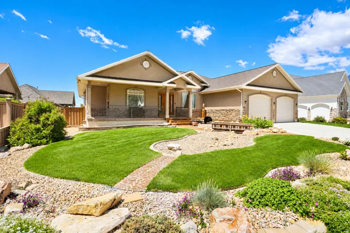 Stucco and stone facade home featuring a covered entry, two-car garage, and a manicured front lawn with a decorative stone pathway and rock landscaping