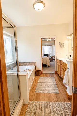 Spacious bathroom featuring wood-finish flooring, a soaking tub with tile surround, and a glass-enclosed shower