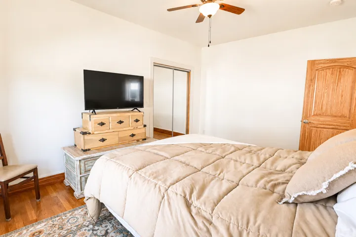 Bedroom featuring wood-finish flooring, a ceiling fan with integrated lighting, and a solid wood paneled door