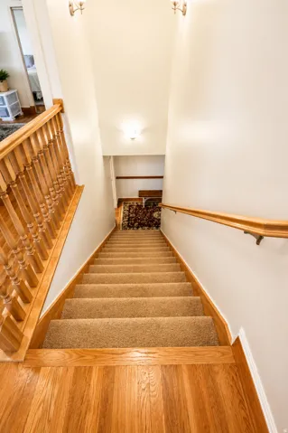 Hardwood flooring at the landing transitions to carpeted stairs, featuring a wood balustrade and handrail