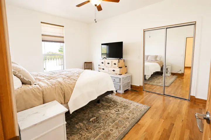 Spacious room featuring wood-finish flooring, a window with a roman shade, and mirrored closet doors