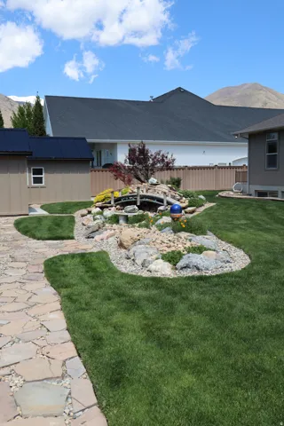 Expansive green lawn featuring a stone pathway, decorative rock garden with a small bridge, and established perimeter plantings