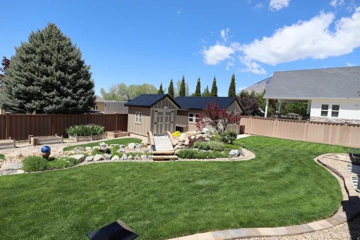 Expansive backyard featuring a lush lawn, decorative rock landscaping, and a wooden bridge structure