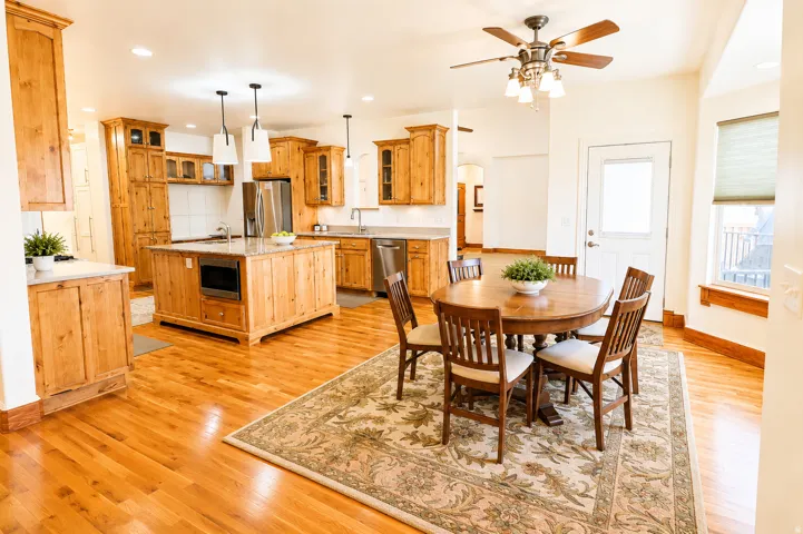Open-concept kitchen and dining area featuring natural wood cabinetry, stainless steel appliances, a center island with built-in microwave, and wood-finish flooring
