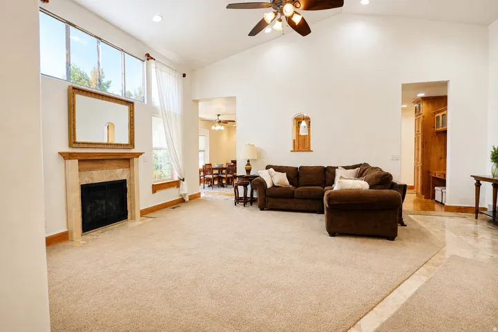 Vaulted living room featuring a fireplace with a stone surround and wood mantel, transom windows, recessed lighting, and a ceiling fan