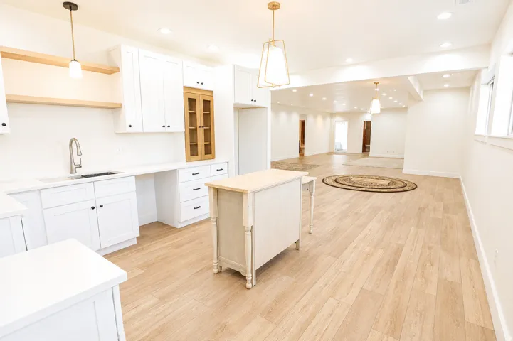 Contemporary kitchen featuring white cabinetry, light wood-finish flooring, a stainless steel sink with a gooseneck faucet, and an accent cabinet with glass panels
