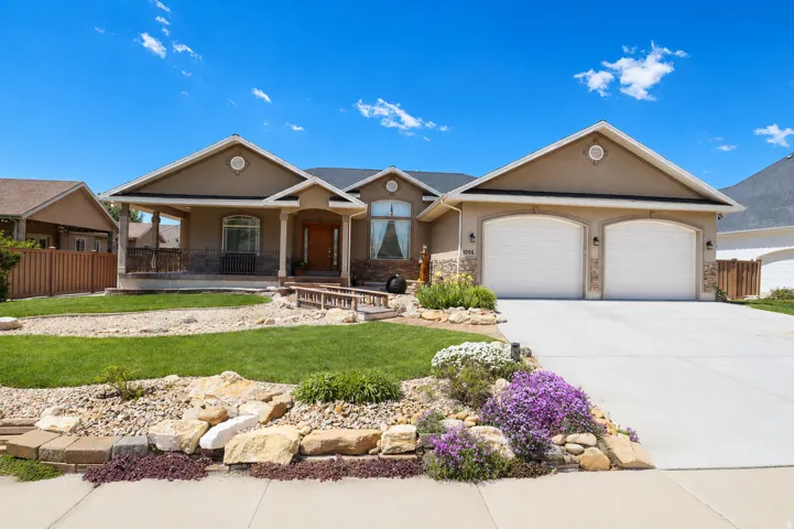 Stucco exterior with a covered front porch, dual garage doors, a concrete driveway, and rock landscaping