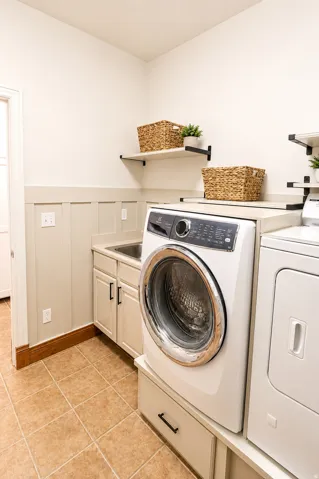 Laundry room featuring a built-in utility sink, light-toned cabinetry with dark hardware, and light-colored wall paneling