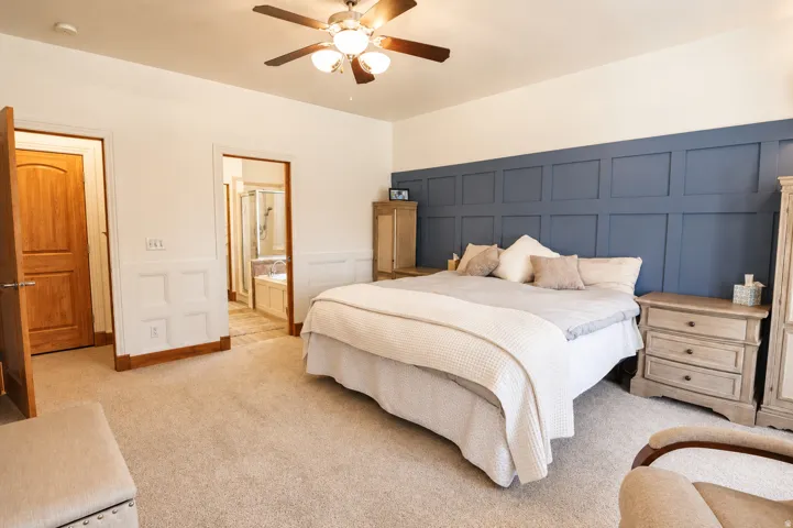 Bedroom featuring a distinctive blue accent wall with panel molding, neutral carpet flooring, and a ceiling fan with integrated lighting
