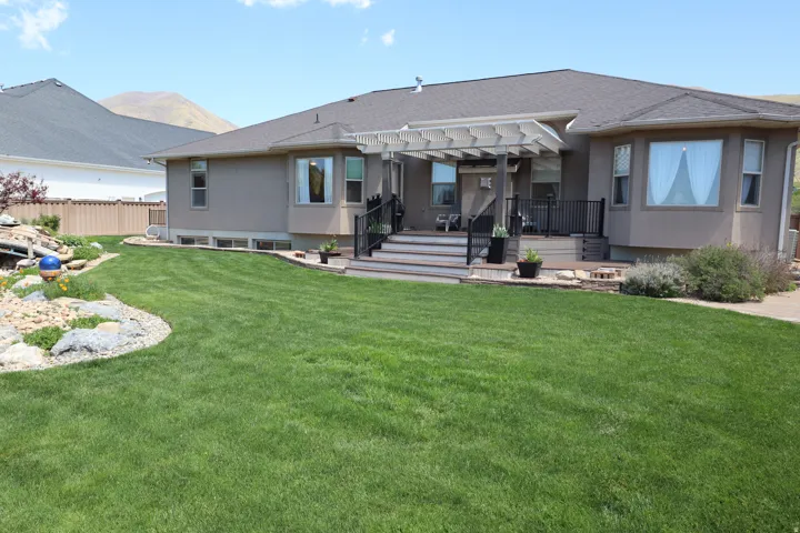 Expansive green lawn with a tiered wood deck featuring black railings and a white pergola