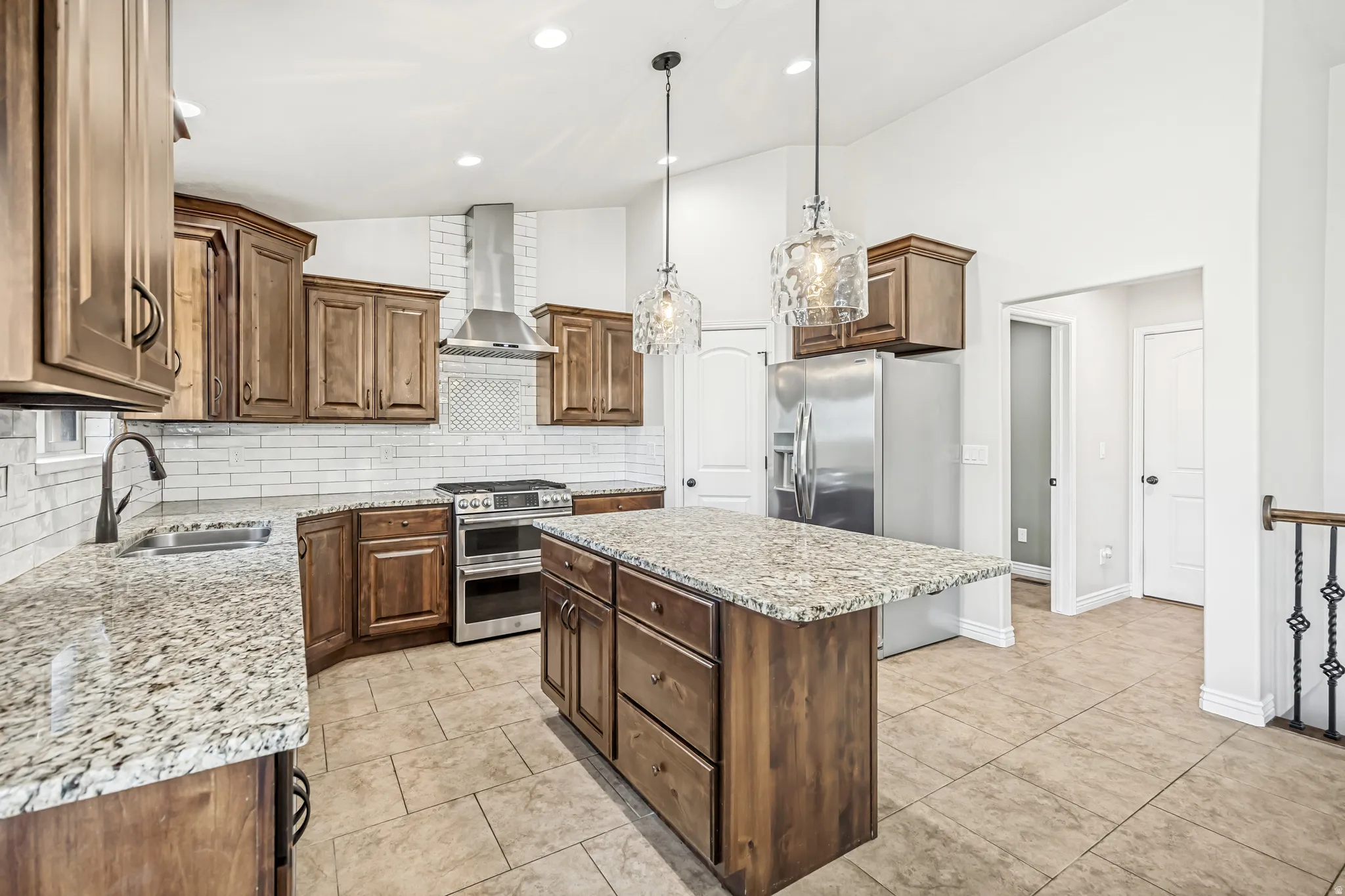 Kitchen with lofted ceiling, stainless steel appliances, light stone counters, a center island, and decorative backsplash