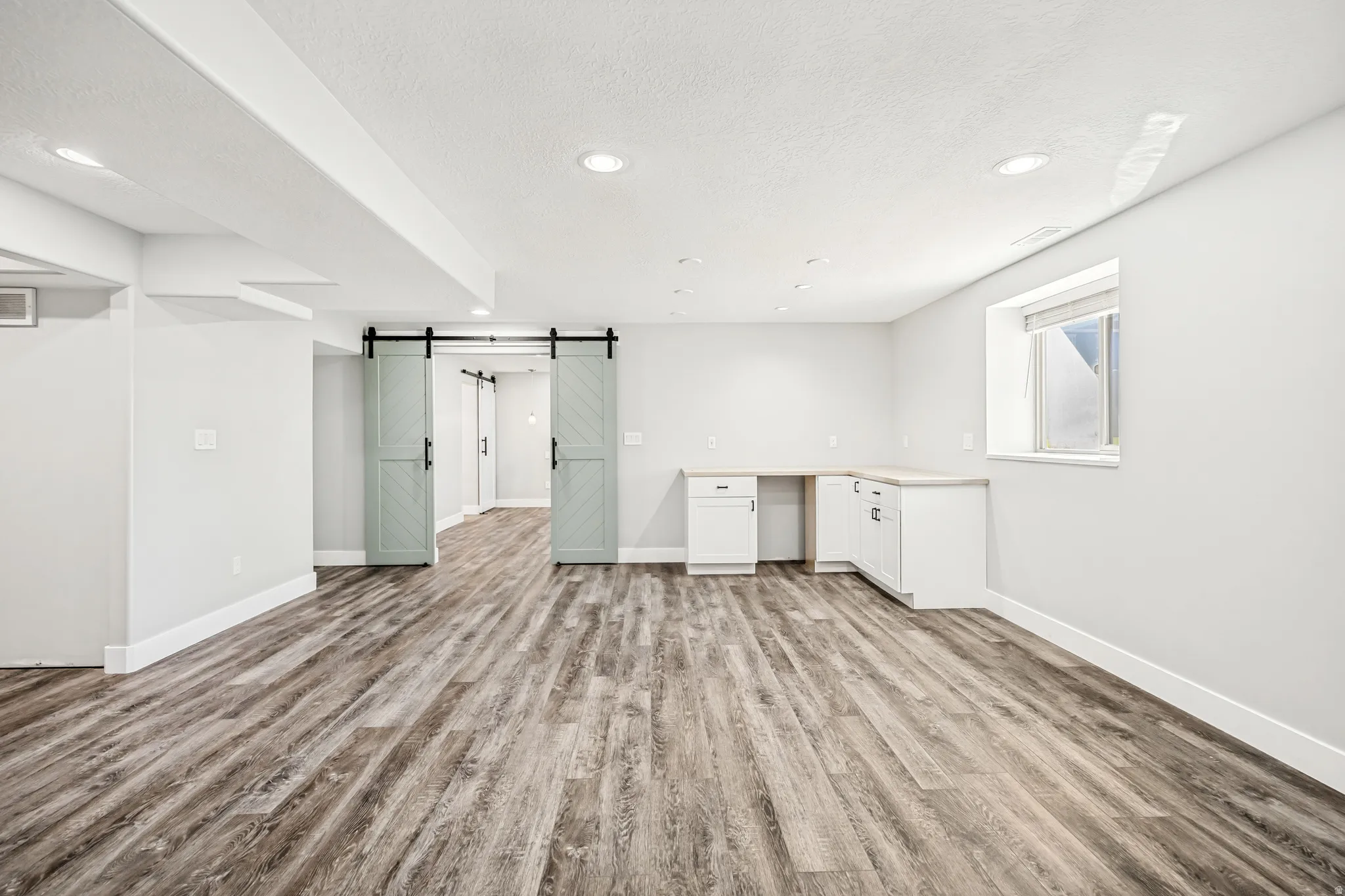Interior space featuring a barn door, light wood finished floors, recessed lighting, a textured ceiling, and built in desk